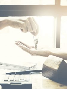 Immobilienmakler gibt Hausschlüssel an Mieter und unterzeichnet Vereinbarung auf Schreibtisch im Büro